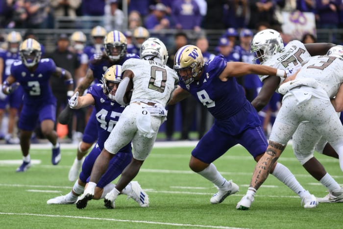an Oregon player holds onto the ball while Bralen Trice reaches his arms out wide to tackle him